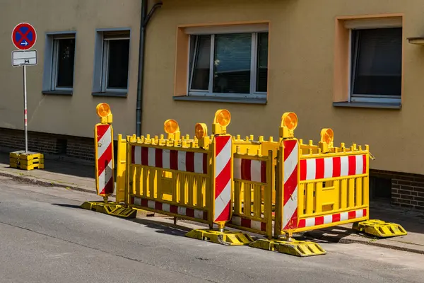 Şehir caddesi boyunca inşaat bariyerleri kurulmuş, devam eden işlerin sinyallerini veriyorlar. Parlak sarı ve kırmızı renkler bariyerleri ayırıyor, güvenlik için net olarak tanımlanmış bir alanı işaretliyor.