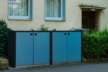 İki mavi depo bir konut binasının dış yüzüne karşı yan yana duruyor. Yeşillik dolapları çerçeveler, doğal cazibesini arttırır..