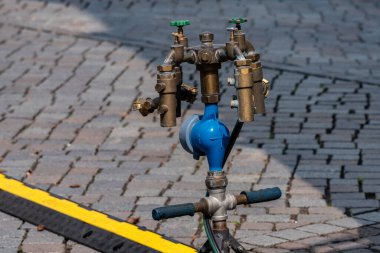 Bir kaldırım taşı caddesine birden fazla pirinç kapakçık ve mavi bir merkez kurulmuş karmaşık bir su tedarik sistemi. Kurulum bölgedeki verimli su dağılımı için tasarlandı..