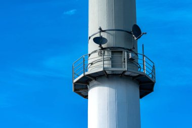 Yüksek bir iletişim kulesi açık mavi gökyüzüne ulaşıyor, çoklu uydu çanaklarıyla donatılmış. Metalik yapısı modern bir tasarım sergiliyor, teknolojiyi ve bağlantıyı vurguluyor.