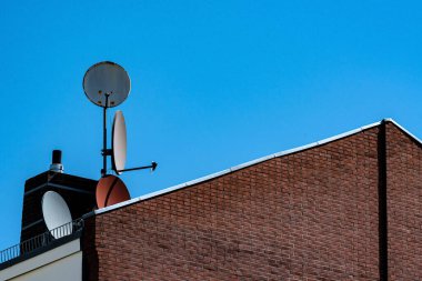 Birkaç uydu anteni tuğla bir binanın çatısına yerleştirildi. Açık mavi gökyüzü geleneksel bir yapıya karşı modern teknolojiyi sergiliyor..
