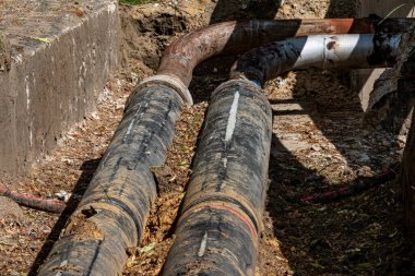 İki büyük, yıpranmış boru toprak ve enkaz ile çevrili bir inşaat sahasında yerde yatıyor. Güneş ışığı parlıyor, malzemelerin dokusunu ve durumunu vurguluyor..
