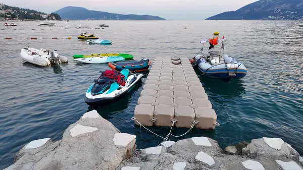 Karadağ 'ın güzel Kotor Körfezi' ndeki Herceg Novi rıhtımında demirlemiş çeşitli su sporları ekipmanlarının canlı bir görüntüsü. Görüntü, jet ski 'leri, şişme botları ve körfezin berrak sularında yavaşça sallanan kanoları gösteriyor.. 