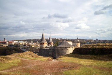Ukrayna 'daki tarihi Kamianet-Podilskyi Kalesi' nin panoramik manzarası. Antik taş duvarları ve kuleleri, bulutlu bir gökyüzünün altında, ortaçağ ihtişamını sergiliyor..