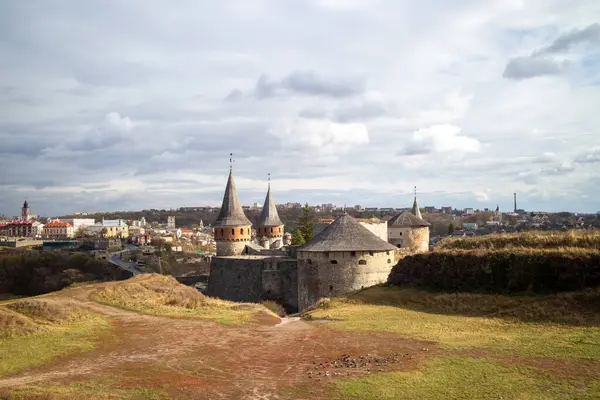 Ukrayna 'daki tarihi Kamianet-Podilskyi Kalesi' nin panoramik manzarası. Antik taş duvarları ve kuleleri, bulutlu bir gökyüzünün altında, ortaçağ ihtişamını sergiliyor..