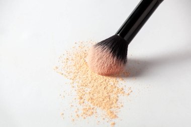 Shattered face powder and cosmetic brush on white background. Make up powder texture close up. Scattered matte powder.