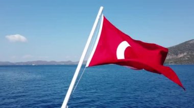 Denize karşı mavi gökyüzünde dalgalanan Türk bayrağı, Türkiye. Bayrak direğinde hindi bayrağı. Kapat.