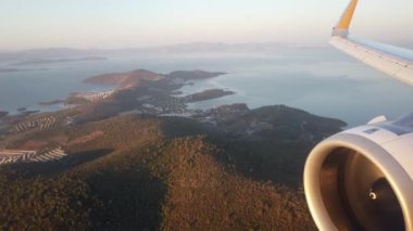 Mavi gökyüzü, şafak vakti lombolik uçaktan kara ve deniz manzarası. Motorlu uçak kanadı. Uçak penceresi görünümü