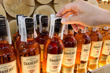 Hand holding Oakheart spiced rum Bacardi 500 ml rum bottle in a supermarket shelf closeup. Ukraine, Kharkiv - july 20, 2023