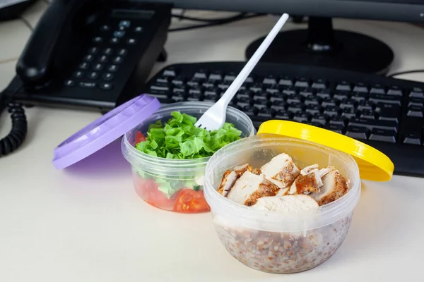 Lunch on work place. Food box container with fresh salad, buckwheat and chicken on the working desk with keyboard