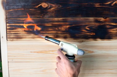 Gaz ocağında yanan ahşap bir tahta. Evde gaz ocağıyla fırçalamak. Tahtanın yumuşak kısmına ateşle yaklaşıyorum. Ahşap ürünlerin dekorasyonu.