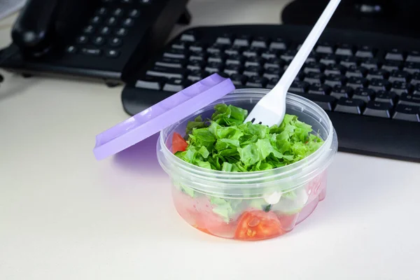 Lunch on work place. Food box container with fresh salad on the working desk with keyboard