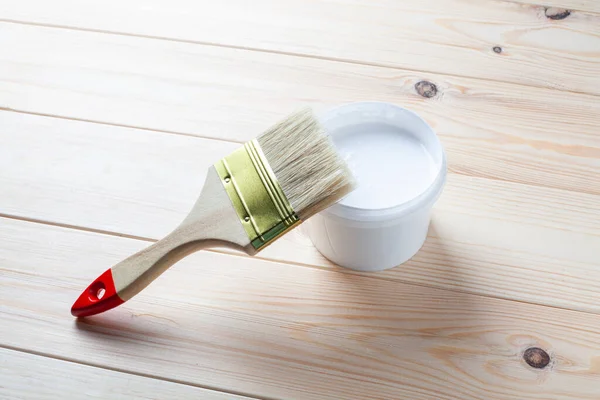 White paint bucket with paint brush on the wooden background.