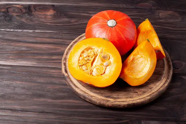 Koyu ahşap arka planda dilimlenmiş balkabağı. Masada kırmızı balkabağı.