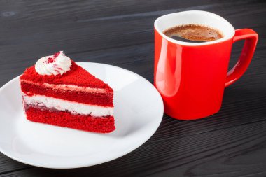 Bir dilim kırmızı kadife kek, ahşap bir masada kremalı beyaz krema ve yanında da dumanı tüten bir kupa aromatik kahve..
