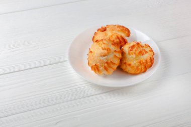 Kremayla dolu altın profiteroller, beyaz masada beyaz tabakta servis ediliyor. Her durum için nefis bir tatlı eşleşmesi..