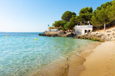 Cala Kontes Koyu, ses Illetes, Mayorka, Balearic Adaları, İspanya. 20 Temmuz 2022 - Kumun yanındaki çam ağacında şemsiyeli bar terası. Çeviri: Balearic School of Cano