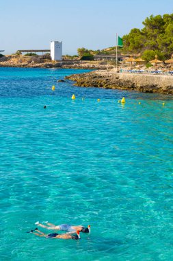 Cala Comtesa cove, Ses Illetes, Majorca, Balearic Islands, Spain. July 20th, 2022 - People snorkeling in the cove, next to the rocky coast with umbrellas and loungers