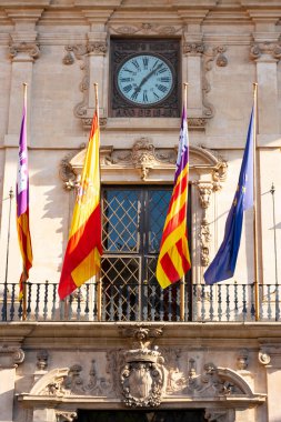 Palma, Mallorca, Balear Adaları, İspanya. 21 Temmuz 2022 - Avrupa Topluluğu, İspanya Topluluğu ve Balear Topluluğu bayrakları ile belediye binasının ön cephesinde saat ve şehrin taş arması ile birlikte balkon