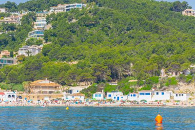 Javea, Alicante, İspanya. 22 Mayıs 2022 - Koyun, Cala Portitxol, küçük bir sahil balıkçı binaları ve tepenin üzerindeki çam ağaçlarının arasında bulunan küçük bir sahil, denizdeki bir tekneden.