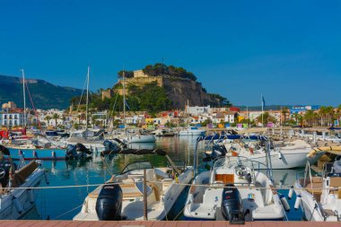 Denia, Alicante, İspanya. 22 Mayıs 2022 'de yelkenliler ve limana demirlemiş diğer tekneler. Arka planda, eski kasabadaki oteller ve restoranlar ve tepenin üstündeki şato.