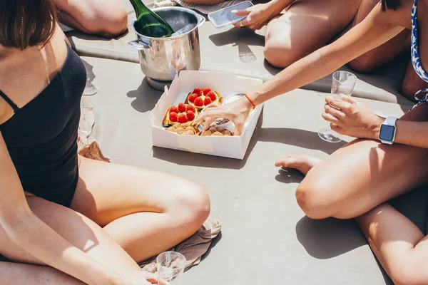 Şampanyalı ve pastalı bir grup genç kadın yazın denizde yelken açan bir teknede eğleniyorlar.