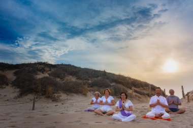 Bir grup kadın ve erkek kumsalda yoga yapıyor. Padmasana veya lotus asana