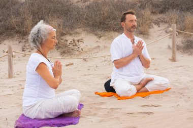 Erkekler ve kadınlar kumsalda kundalini yogası yapıyorlar. Dua pozu