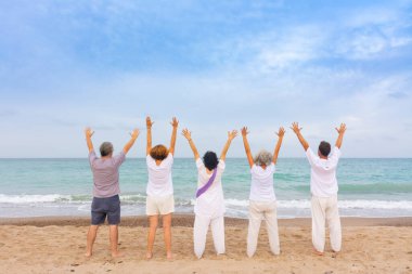 Bir grup kadın ve erkek, kumsalda kumda kundalini yogası yapıyor. Duruş