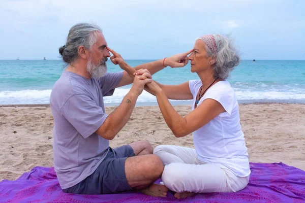 Couple meditating together in a sitting position favoring the personal relationship by touching each other on the beach