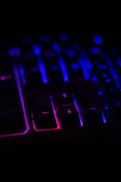 Backlit keyboard of a personal computer, with out-of-focus keys, on a dark background of a desk at night