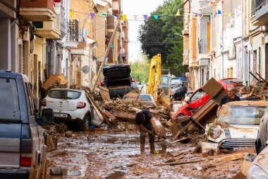 Massanassa, Valencia, İspanya. 31 Ekim 2024 'te, selden sonra biri evinden çıkarılan bir kova çamuru sokağa boşalttı. Sokakta araba ve enkaz var.