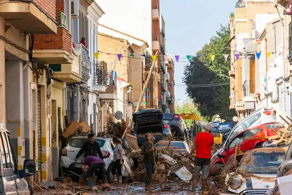 Massanassa, Valencia, İspanya. 31 Ekim 2024 - Bölgedeki sellerin ardından, insanlar temizlik ve enkaz temizleme işlerini yaparken, kasabada yığılmış araçlarla dolu bir cadde ortaya çıktı..