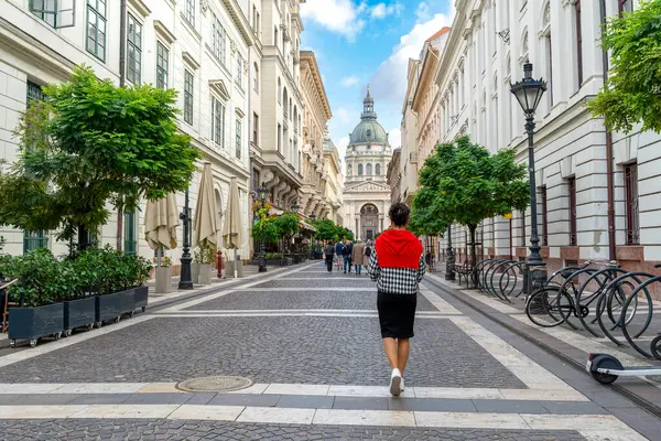 Zarif bir kadın Budapeşte, Macaristan 'daki Aziz Stephen Bazilikası' na doğru yürüyor, yemyeşil ve berrak bir gökyüzü var..