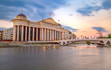 Şehir merkezinde Makedonya Arkeoloji Müzesi ve Medeniyetler Köprüsü. Vardar Nehri 'nin sakin suları ve canlı bir günbatımı görüntüsü..