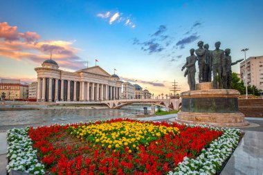 Kuzey Makedonya 'nın başkentinin güzel bahar kenti - Üsküp ve Arkeoloji Müzesi. Sanat ve Anıtlar Köprüsü manzarası. Önplanda renkli çiçekler.
