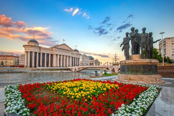 Kuzey Makedonya 'nın başkentinin güzel bahar kenti - Üsküp ve Arkeoloji Müzesi. Sanat ve Anıtlar Köprüsü manzarası. Önplanda renkli çiçekler.