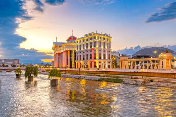 Üsküp 'te güzel bir günbatımı ve Vardar nehrinde ışık yansıması. Makedonya Arkeoloji Müzesi ve Medeniyetler Köprüsü gün batımında.