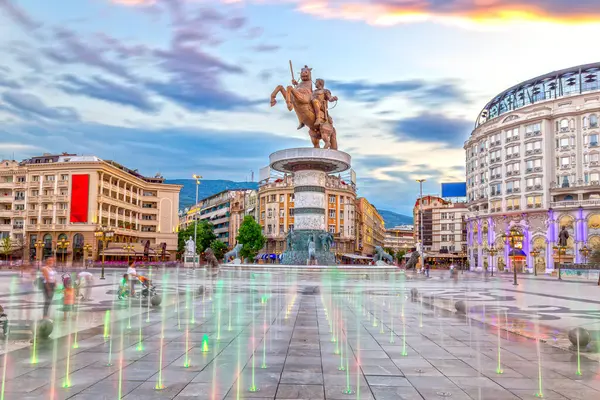 Gün batımında Üsküp 'teki Makedonya Meydanı' nda dans eden fıskiyeler ve Büyük İskender heykeli (At Savaşçısı) arka planda