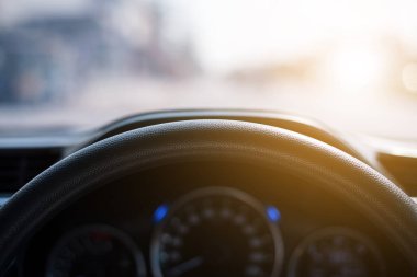 Günbatımının arka planına sahip arabanın direksiyonuna yakın çekim. Yol manzarası, arabanın ön camından görüntü. Şehir yolunda gün batımında araba sürerken.