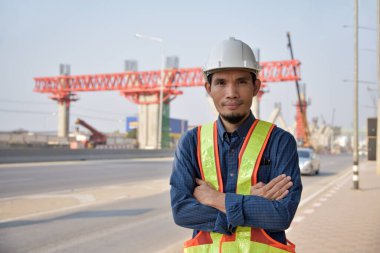 Asyalı erkek inşaat mühendisi bir inşaat alanında kollarını kavuşturmuş duruyor..