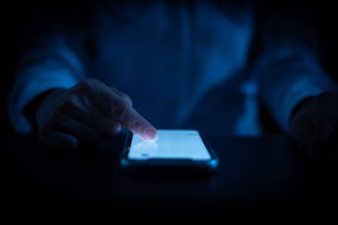 Geceleri cep telefonuyla çalışan bir kadın, karanlık geçmişi olan bir akıllı telefona dokunan bir parmak.