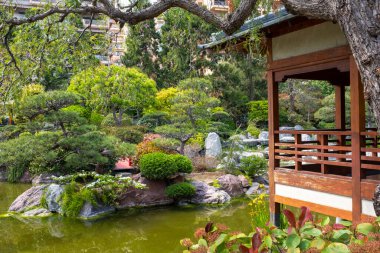 Monako - 3 Mayıs 2022: Bir ahşap pavyon Monako Japon bahçesinin göletine bakıyor. Güneşli bir bahar gününde çekilmiş.