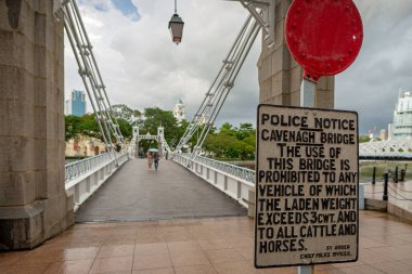 Singapore - December 20, 2022: Old fashion sign at the entrance of the Cavenagh bridge. Taken on a rainy day with an unrecognizable couple walking with an umbrella in the distance clipart