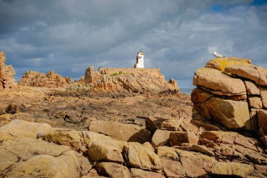 The peacock lighthouse (phare du Paon) and red cliffs in the foreground. Taken on a partly sunny summer day, Brehat Island, Brittany, France. clipart