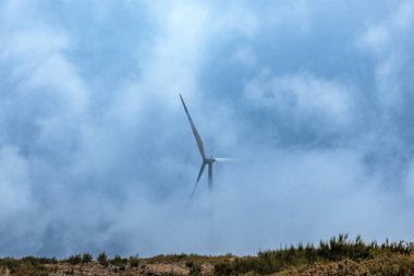 Portekiz 'in Madeira adasında sisli dağların tepesinde bir rüzgar türbini.