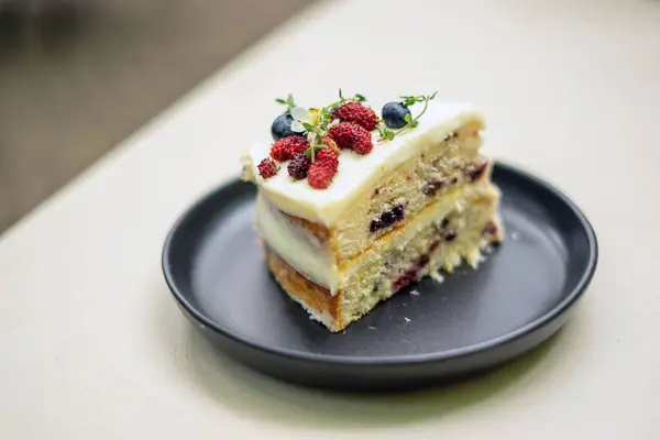 A slice of Vanilla Mixed Berry Cake adorned with mulberries on top, revealing the layers of mixed berries and cream, as well as the soft, tender cake beneath.