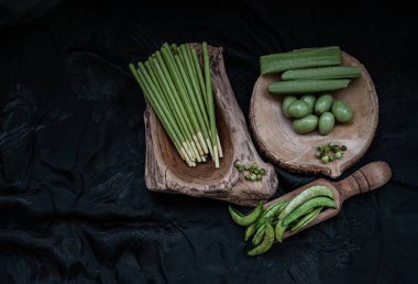 Değişik tatlara sahip yeşil atıştırmalıklar ve farklı şekillerde kavrulmuş bezelye, bisküvi kaplı Matcha kremalı bisküvi çubukları, Matcha latte krep kurabiyesi ve ahşap bir tabakaya serilmiş bademler. Yeşil Tatlılar