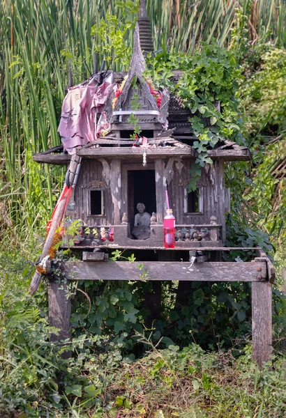 A old wooden spirit house or Joss house built for guardian spirit to reside for protective spirit of a place On the overgrown grass beside the road. and Red soft drink is the belief of Thai villagers. Selective focus.