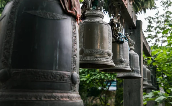 Many metallic bells hanging in a row on wooden pillars outside in thai buddhist temple. Lined with many beautiful bells, Thai temple bell which believe that who knock this bell will get the good luck, Image with shallow depth of field, No focus, spec